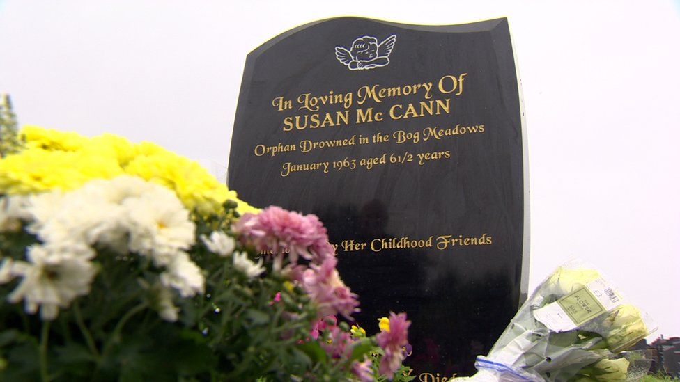 The newly installed gravestone for Susan McCann. The inscription says in loving memory of Susan McCann, orphan drowned in the Bog Meadows, January 1963 aged 6 and a half. Remembered by her childhood friends. There are flowers in the foreground.