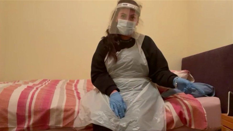 Care worker in PPE sits on bed