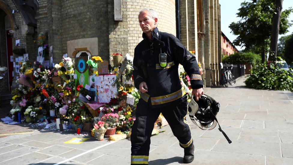 A member of the London Fire Brigade walks past tributes left for the victims