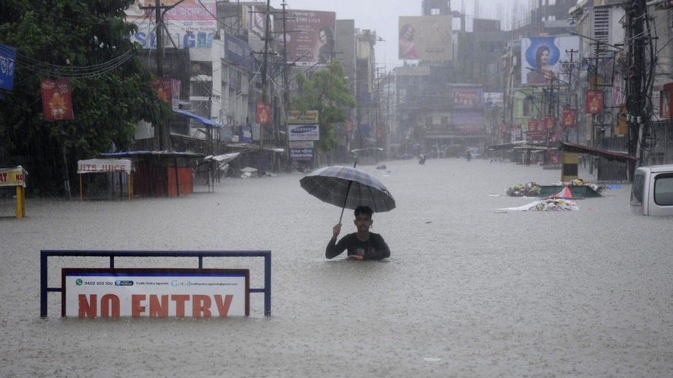 An Indian man holding an umbrella struggles along a flooded street in Agartala, Tripura.