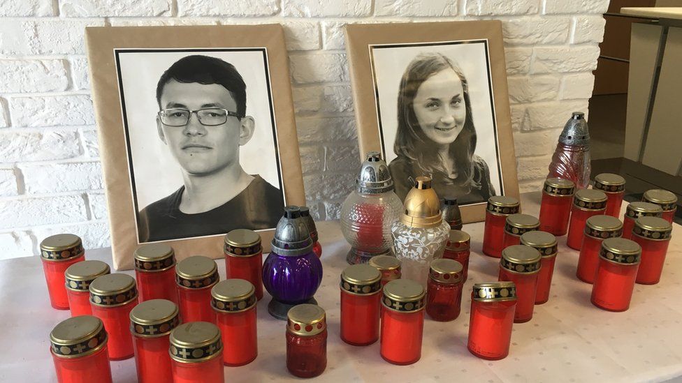 A table, covered in white linen, supports more than a dozen red candles alongside the two photos of Jan Kuciak and his fiancée