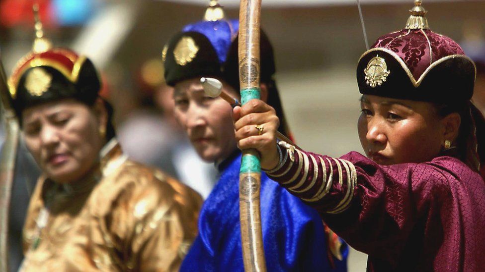 Women dressed in traditional Mongolian clothing compete against each other in archery matches