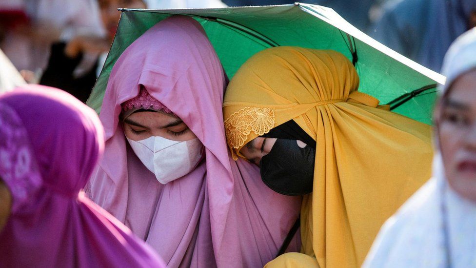 Two women take cover under an umbrella, wearing masks, in Manila, Philippines.