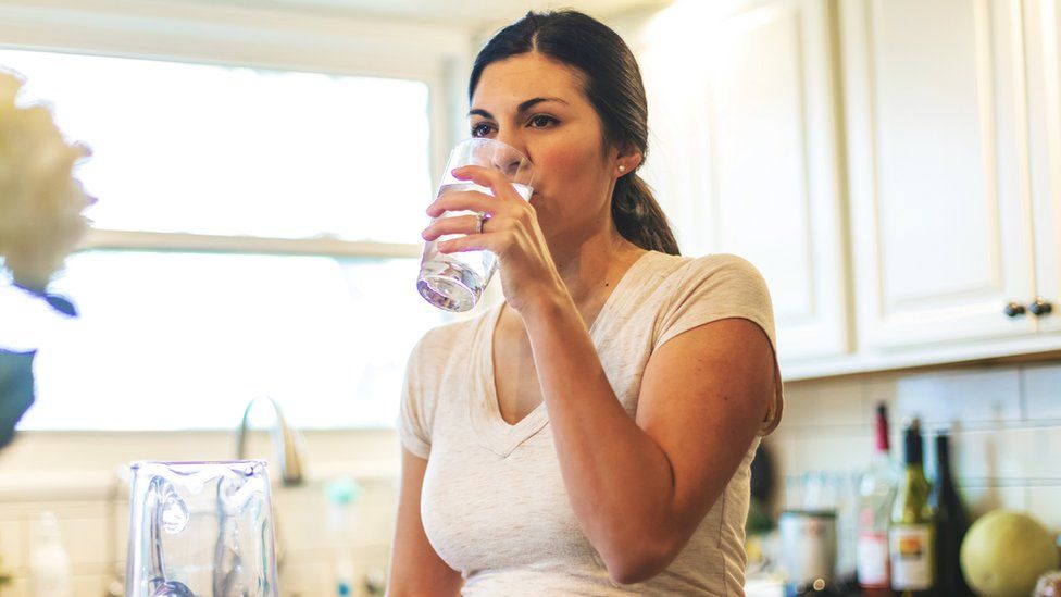 Women stands in kitchen drinking tap water from a glass