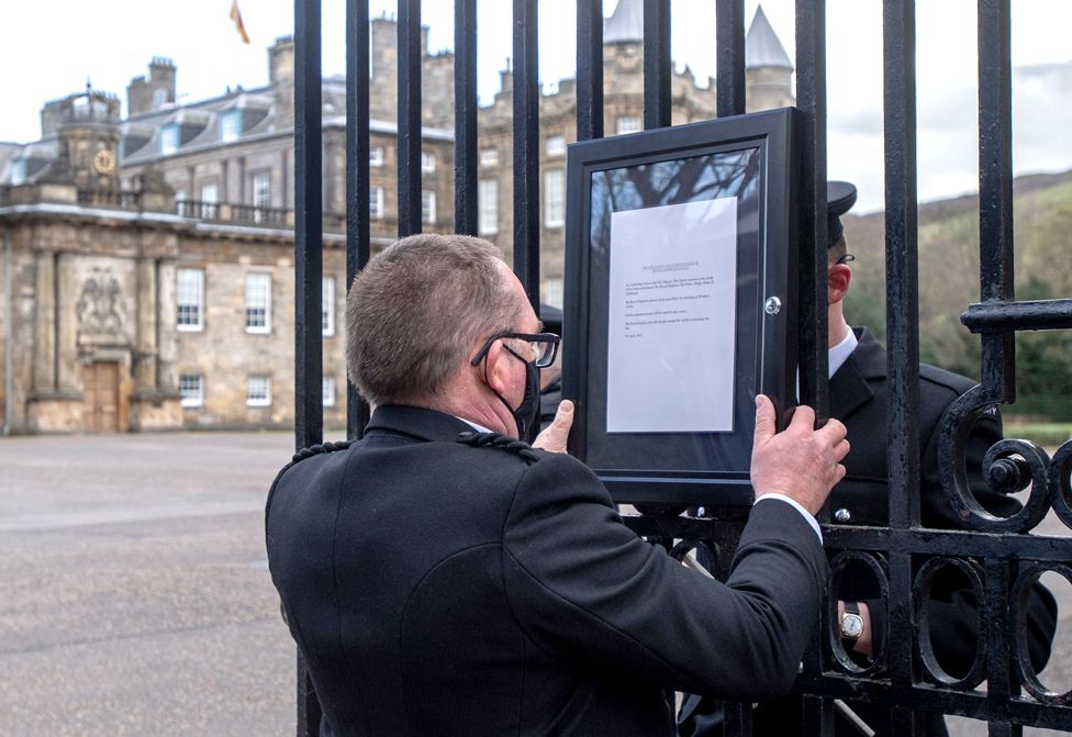 A member of staff attaches a notice to the gates of the Palace of Holyrood house in Edinburgh