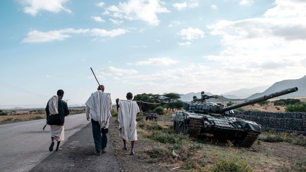 Люди идут рядом с заброшенным танком, принадлежащим силам Тыграя, к югу от города Мехони, Эфиопия - 11 декабря 2020 года
