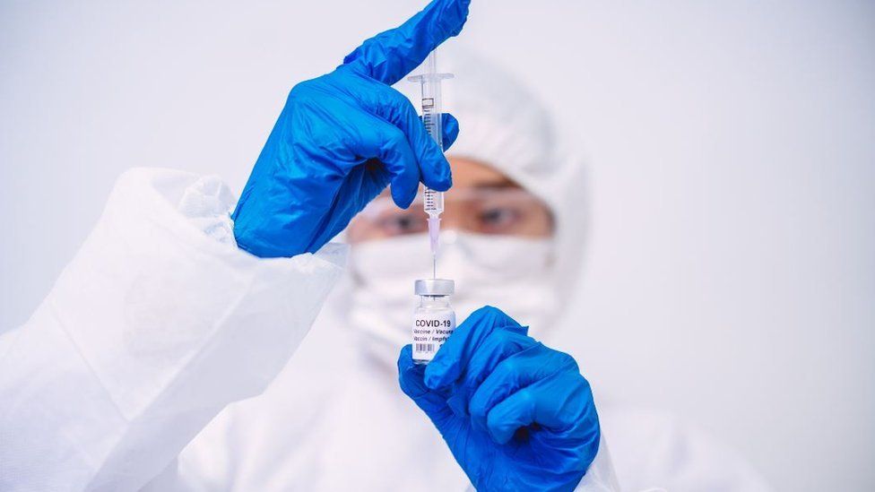 Doctor in protective gloves and workwear filling injection syringe with Covid-19 vaccine - stock photo