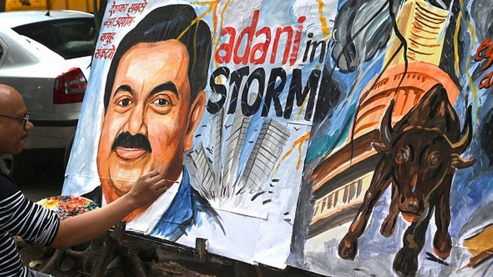 L'insegnante di scuola d'arte Sagar Kambli dà gli ultimi ritocchi a un dipinto dell'uomo d'affari indiano Gautam Adani (L) che evidenzia la crisi in corso del gruppo Adani a Mumbai il 3 febbraio 2023.