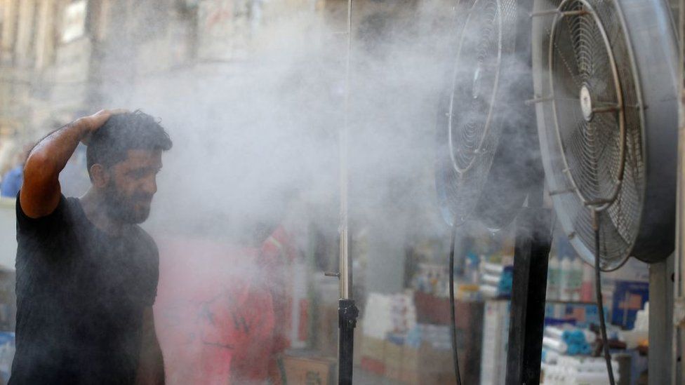 A man cools down in front of a misting fan in Baghdad in July 2022