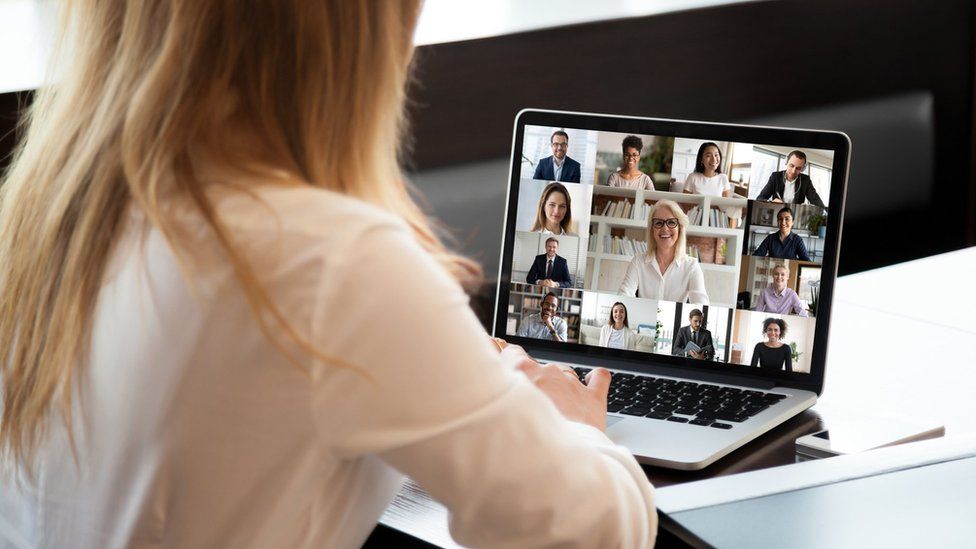 Woman taking part in video conference with laptop showing several faces