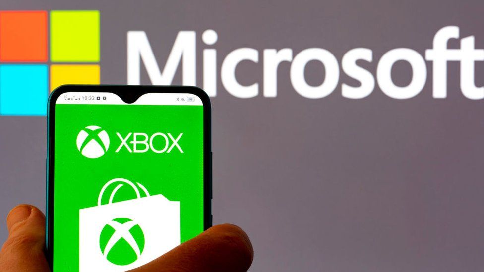 Microsoft logo with someone holding a phone with the Xbox logo.