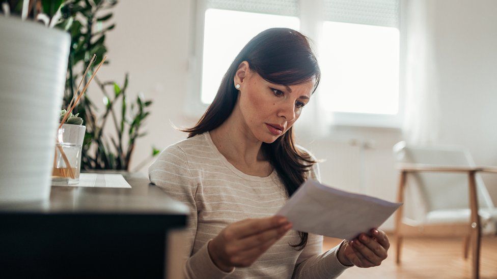 Woman looks concerned reading sheet of paper.