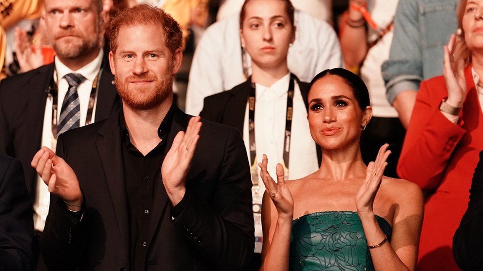 An image showing Prince Harry and Meghan clapping in a crowd