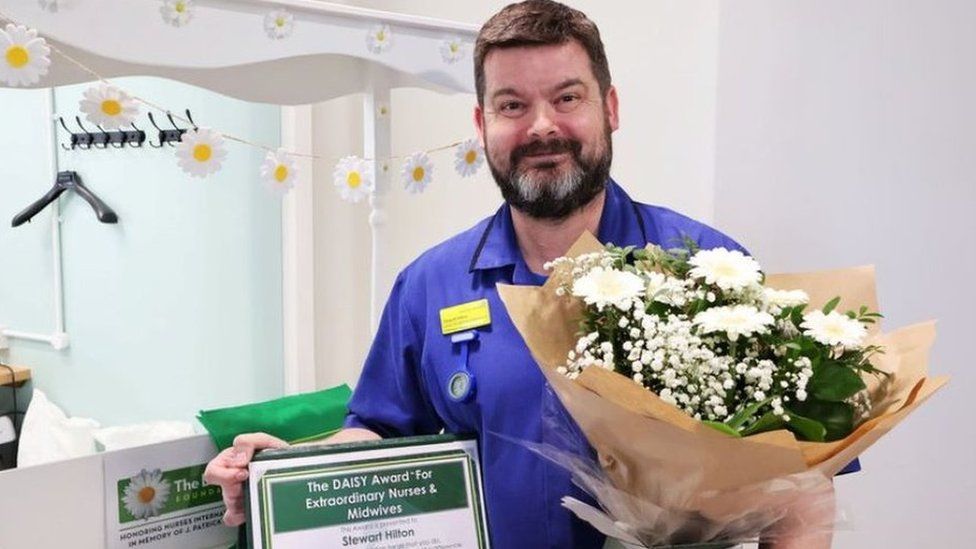 Stewart Hilton pictured in his scrubs holding an award and clutching a bouquet of flowers