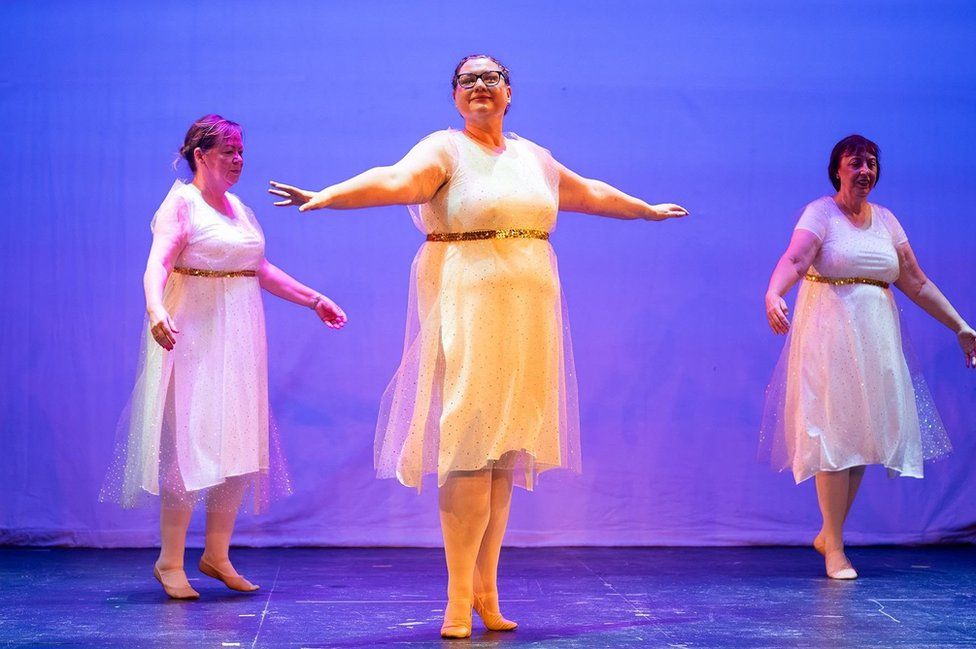 Three women in white dresses do ballet