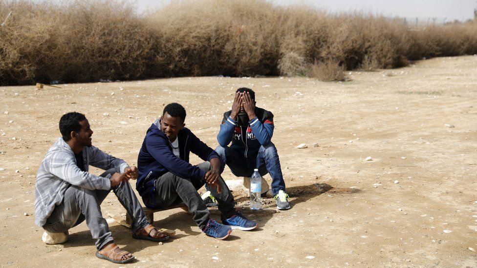 Three African men sit outside Holot detention facility near the Israeli-Egyptian border in southern Israel, 22 February 2018