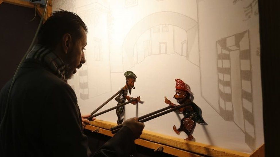 Syrian last shadow puppeteer Shadi al-Hallaq is seen moving his puppets Karakoz (R) and Eiwaz (L) from inside his booth during a presentation in Damascus on 3 December 2018. -