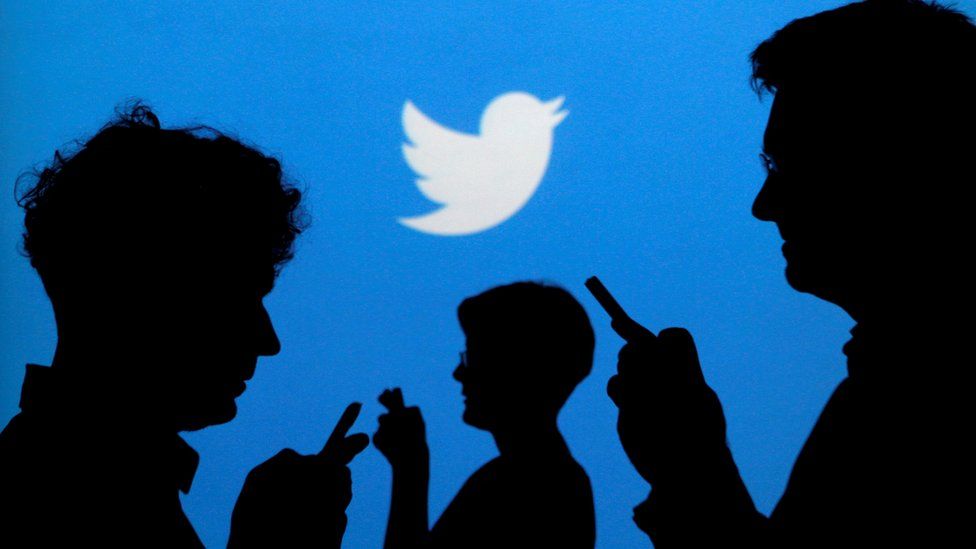 Silhouettes look at phones with the Twitter logo in the background