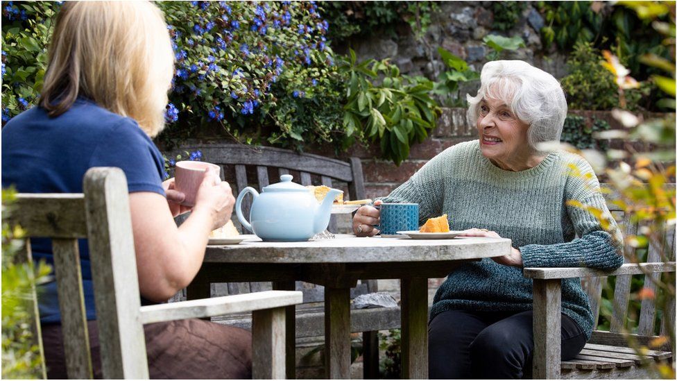 Пенсионерка беседует с родственником за чаем