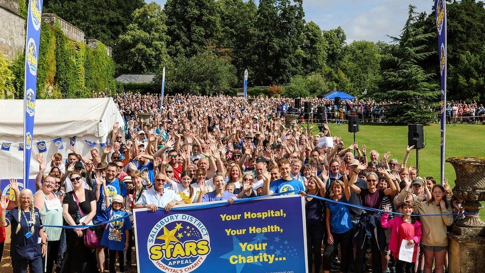 large group of people waving at the camera ready to start walking with a Stars Appeal banner in front of them.