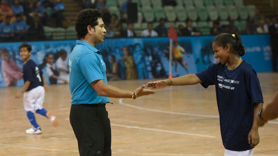 Former Indian cricketer Sachin Tendulkar shakes hand with a young girl during a friendly football match with children from the Special Olympics on the occasion of World Children's Day