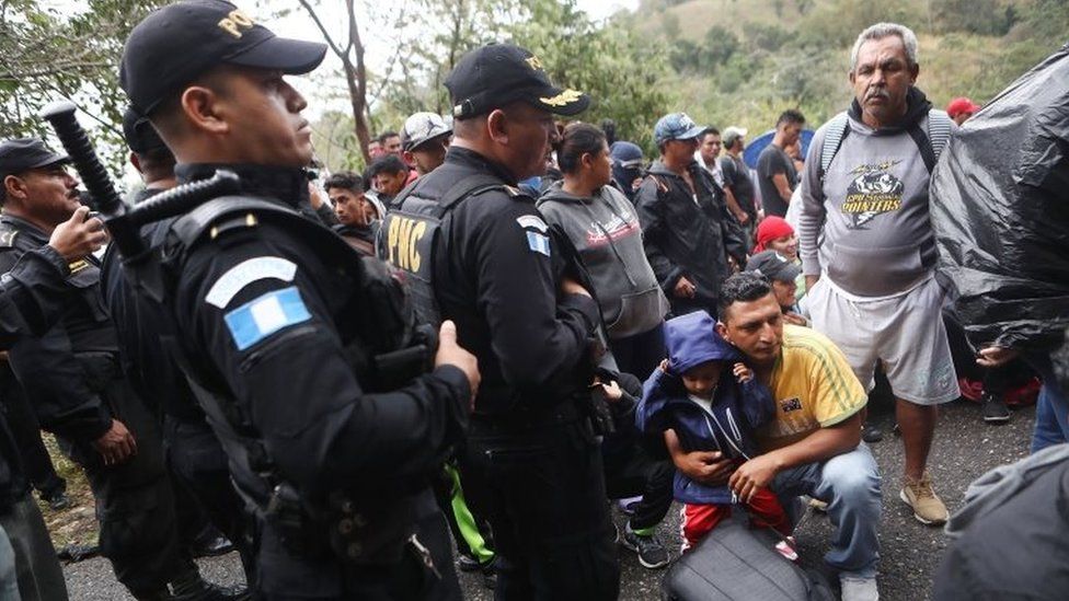 Honduran migrants wait as police block a road to a border checkpoint into Guatemala on 16 January, 2019 in Agua Caliente,