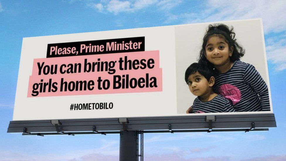 A HometoBilo campaign billboard shows a picture of the two girls next to the message: "Please, Prime Minister, You can bring these girls home to Biloela"