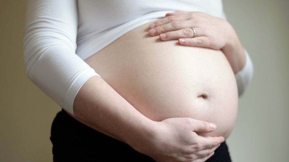 File photo of a woman wearing a white shirt holding a pregnant stomach.