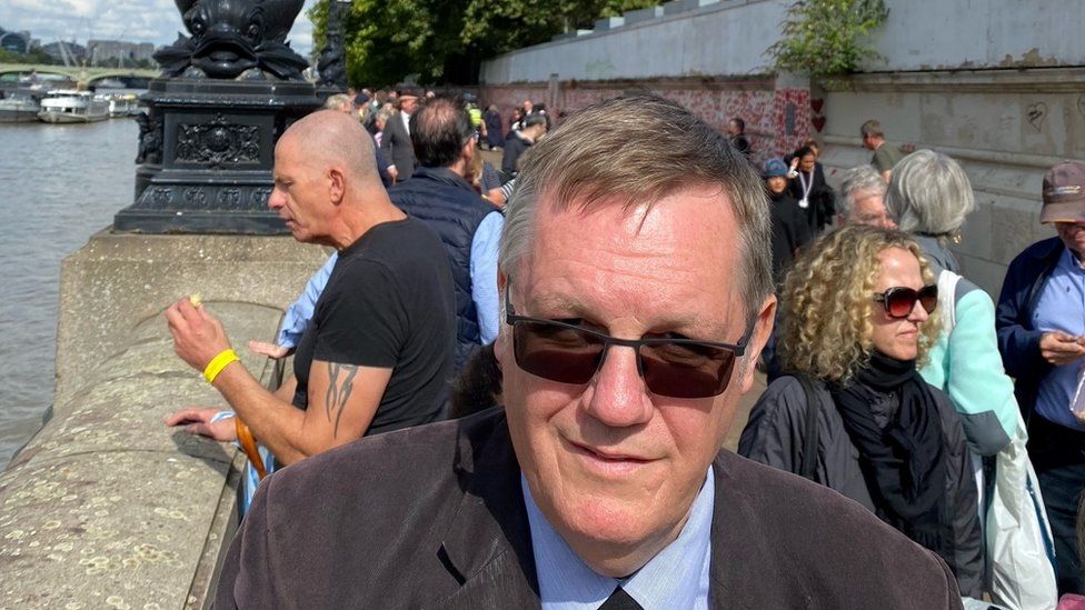 Ian Sherwood standing in queue opposite Westminster