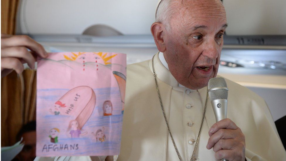 Pope Francis holds up a drawing given to him by a migrant girl