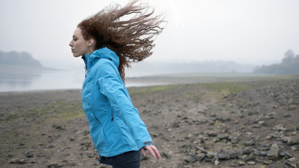 woman stood on beach with winds blowing hair back