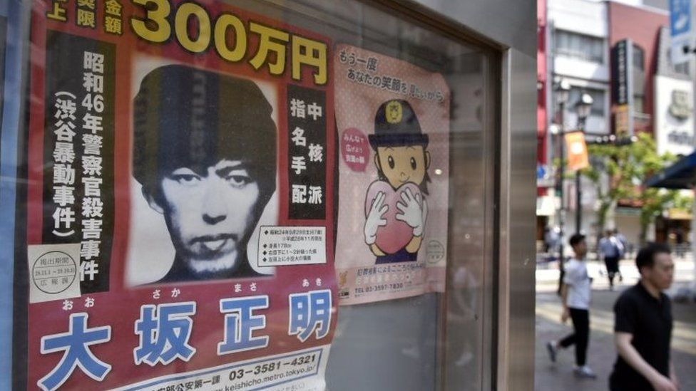 Pedestrians walk past a wanted poster of fugitive Masaaki Osaka (left) displayed at a police box in Tokyo (23 May 2017)