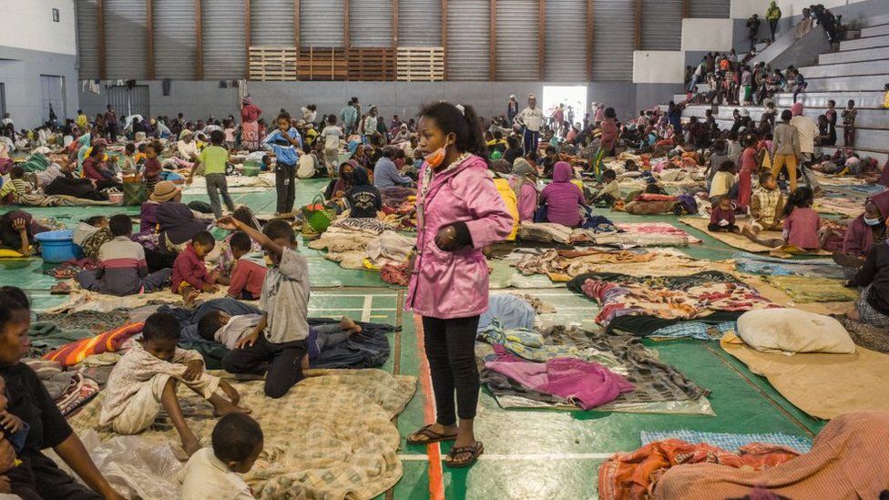 A few hundred people lie on mats on the ground or walk through an indoor sports court