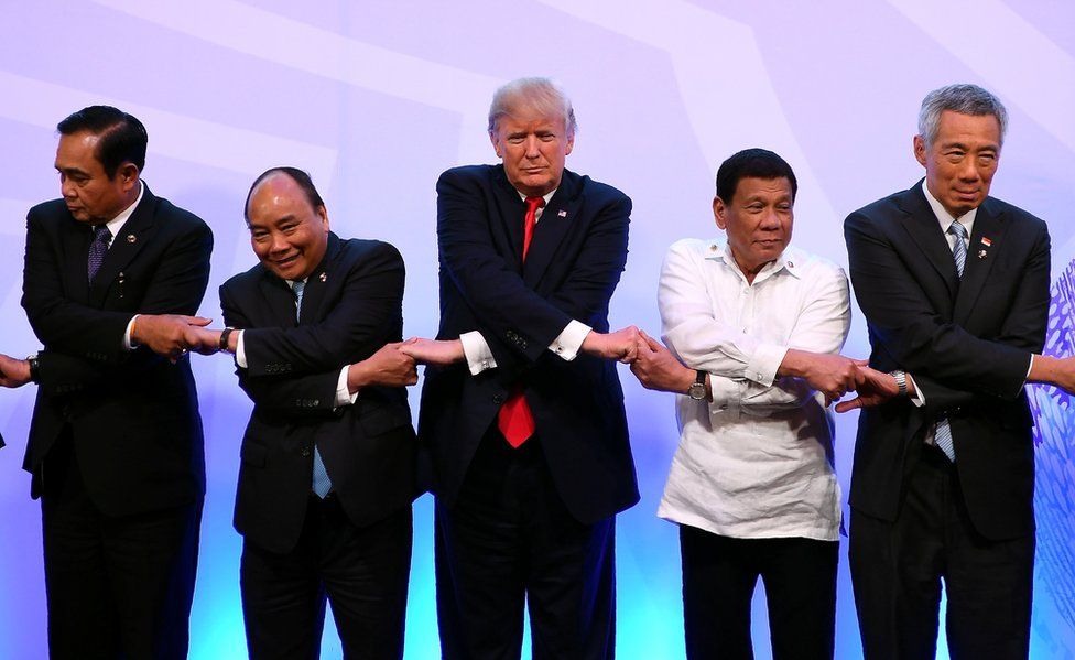 President Donald Trump holds hands with a row of leaders.