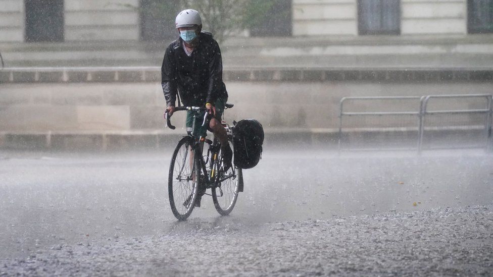 A cyclist rides through flood water in Horse Guards Road in central London