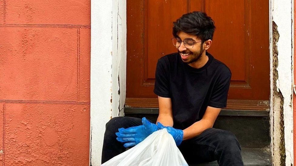 Young man wearing a black t-shirt, sat down with a rubbish back in his hands