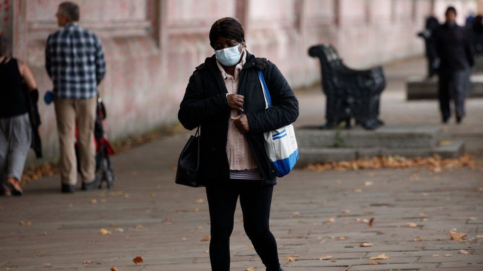 A woman in a mask walks in front of the Covid memorial wall in London