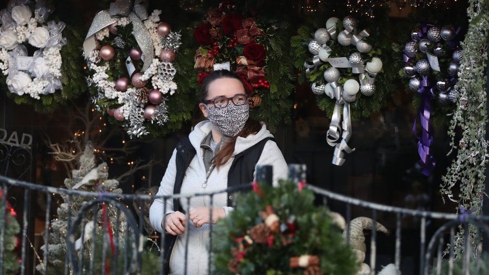 A person wearing a face covering walks passed Christmas wreaths for sale at All Occasions Designer florist in Denny.