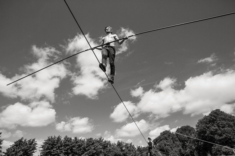 A man walks along a tightrope holding a large pole