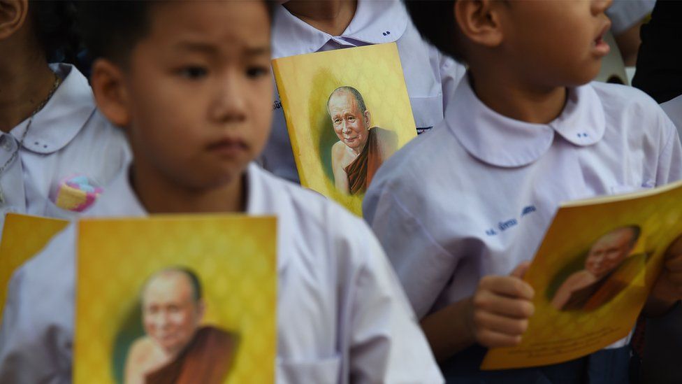 Children hold booklets carrying pictures of Thailand's most senior Buddhist monk, the late Supreme Patriarch Somdet Phra Nyanasamvara