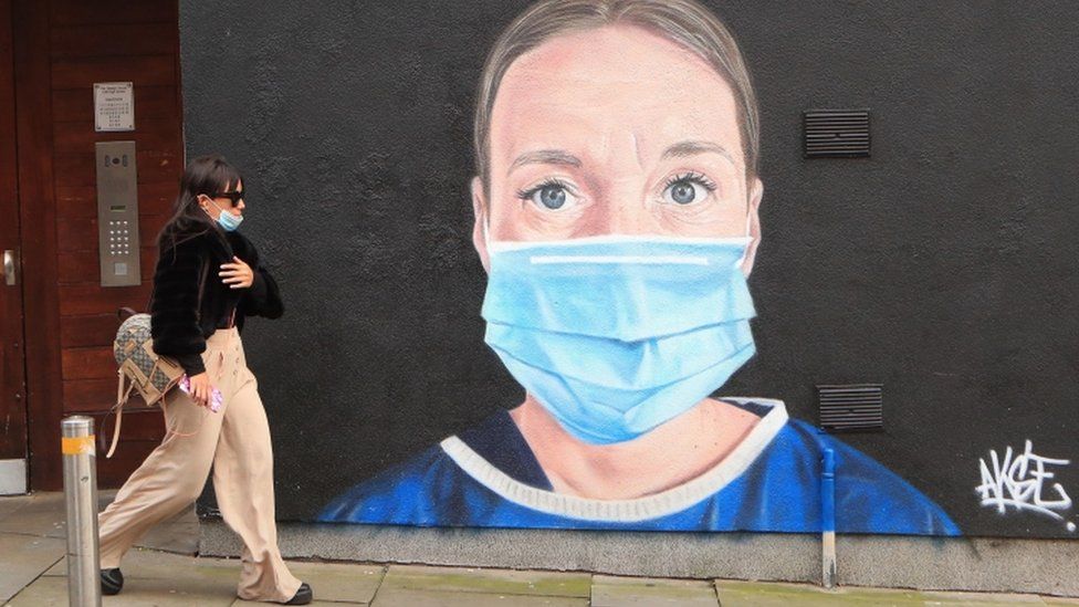 A woman walks past a mural of an NHS worker in central Manchester