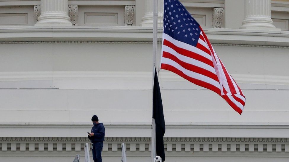 A worker walks under an American flag flown at half staff at the US Capitol