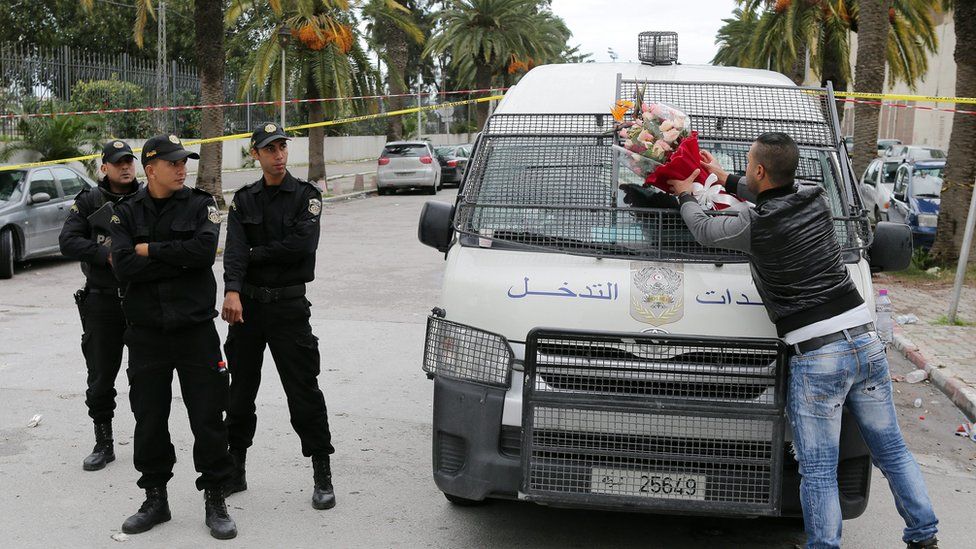 A plain-clothed policeman (R) puts flowers he received from civilian on a police vehicle at the site of a bomb attack on a bus transporting Tunisian presidential guards