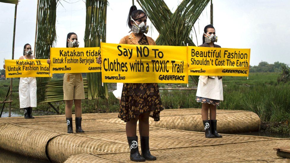 Greenpeace protestors in fashion outfits in Indonesia holding signs that say 'say no to clothes with a toxic trail' and 'beautiful fashion shouldn't cost the earth'
