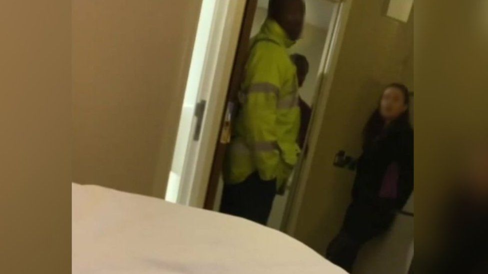 A still from a video clip showing a blurred female member of staff and blurred male security guard stood in the doorway of a hotel room