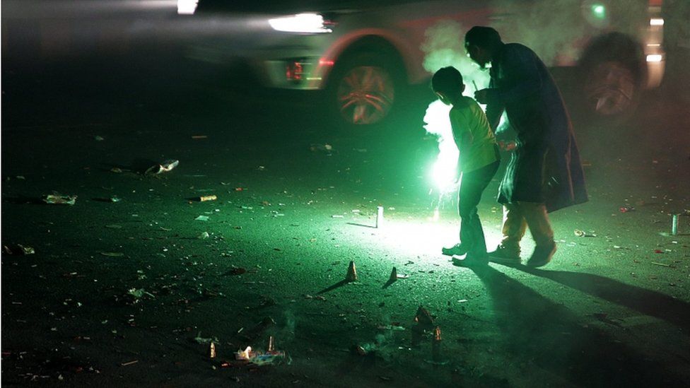 A man helps a child light a firecracker amid traffic on a street littered with spent crackers during the Diwali festival celebrations near New Delhi, India, 30 October 2016