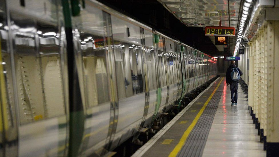 A man walks alongside a stationary train on an empty platform at London Victoria