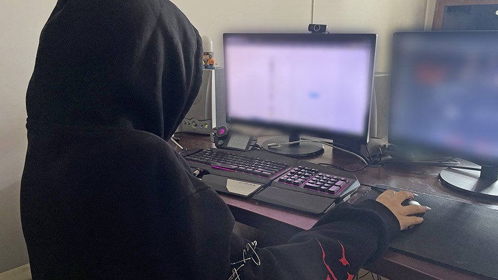 Young person wearing hoodie looks at computer screens