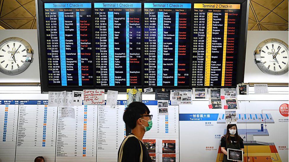 protester walks past an electronic board showing cancelled flights