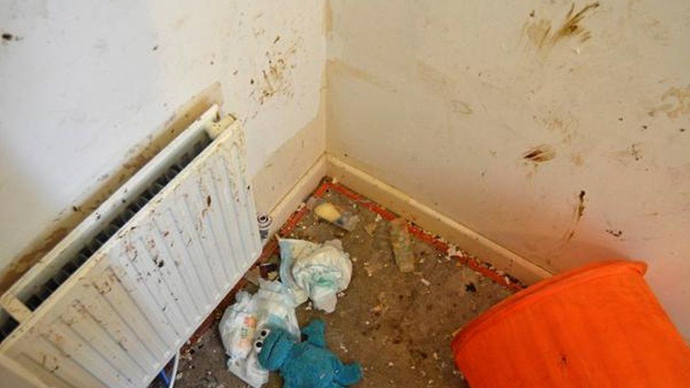 A child's room with faeces on the wall and dirty nappies strewn across the floor